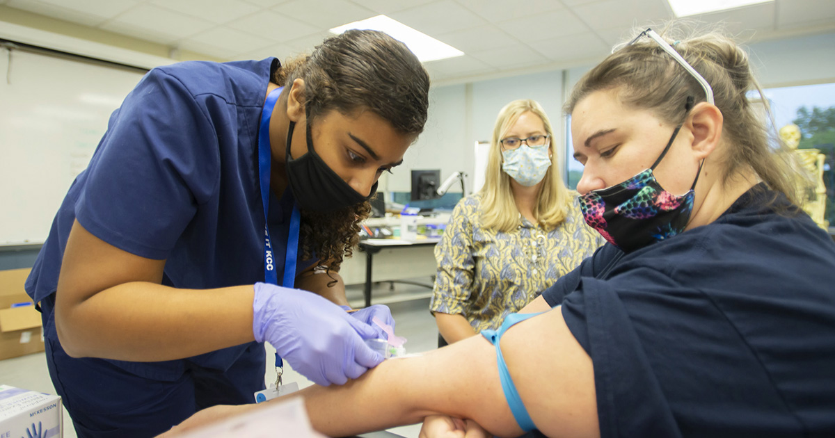 A phlebotomy student takes blood during class.