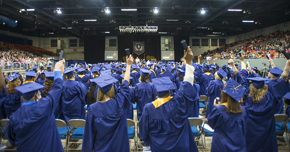 Students raise their diploma tubes during a commencement ceremony.