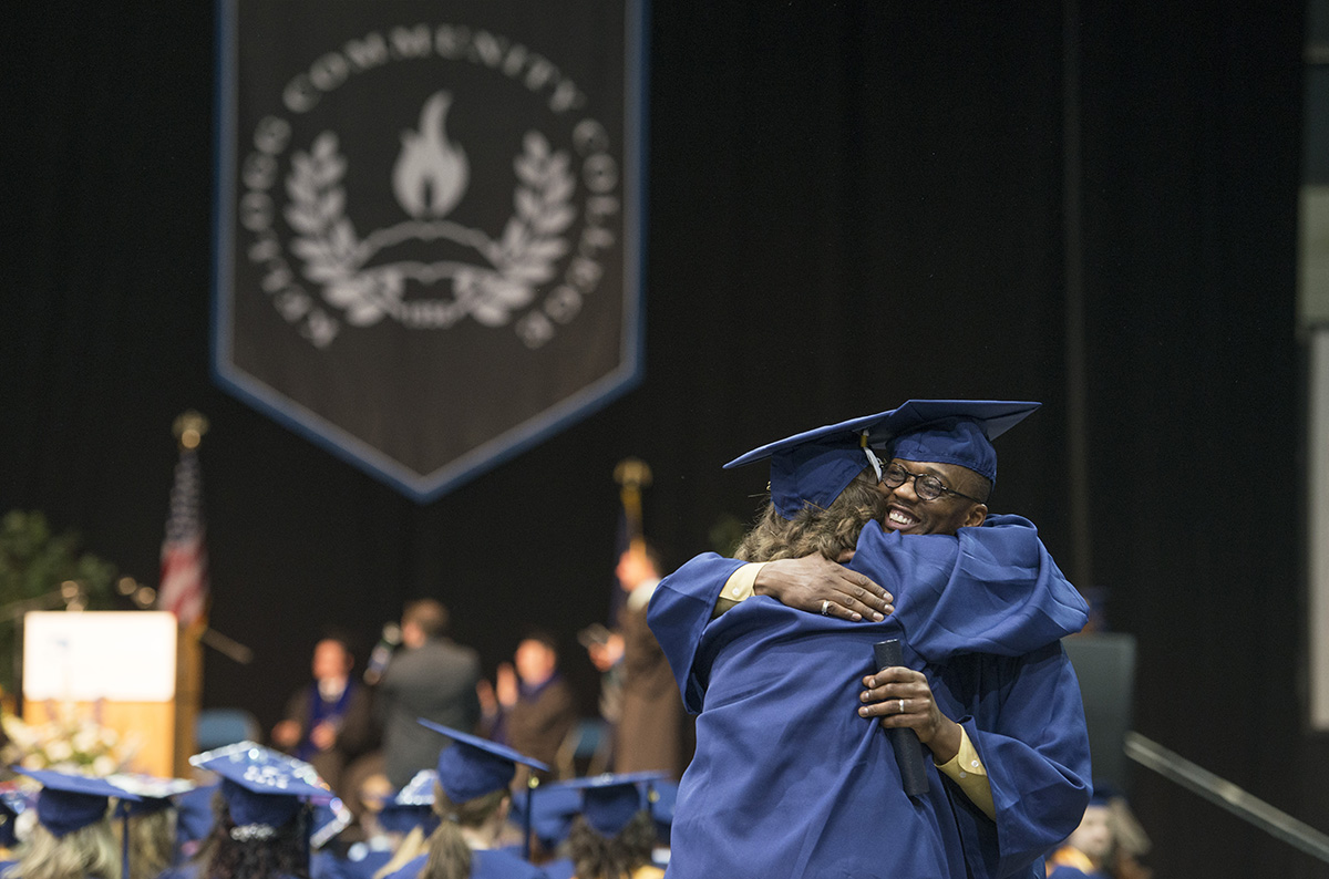 A graduate hugs a faculty member during commencement.