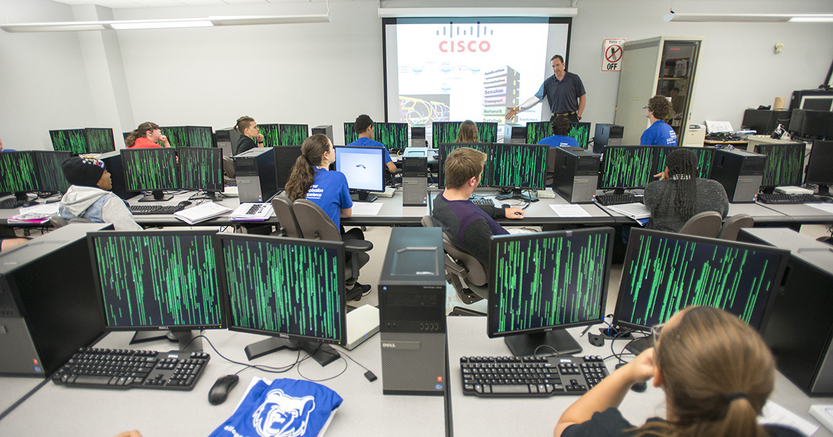 Students listen to an instructor in a computer lab.