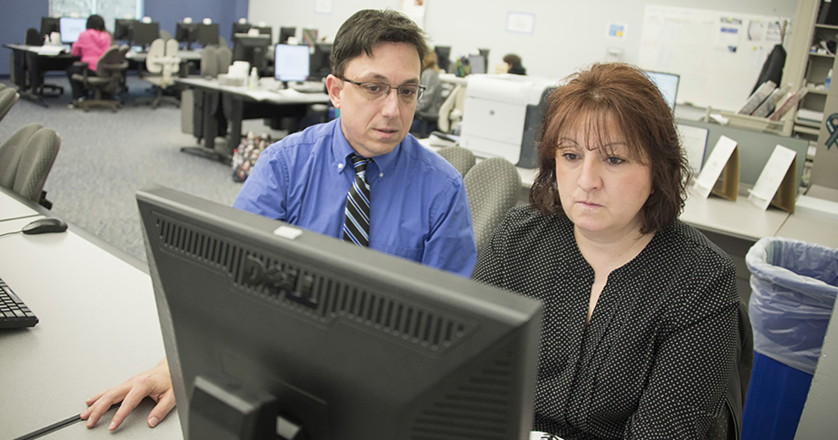 An instructor works with a student in a computer lab.
