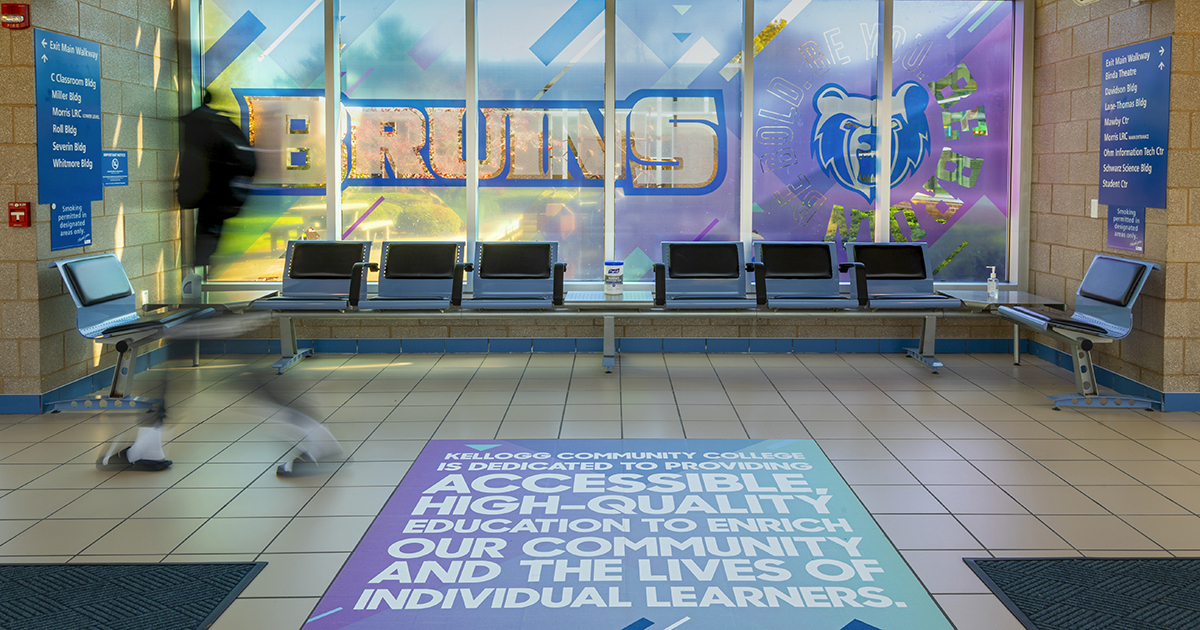 Colorful window clings and floor graphics in the KCC walkway reading "Bruins" along with a stylized version of the KCC mission statement.