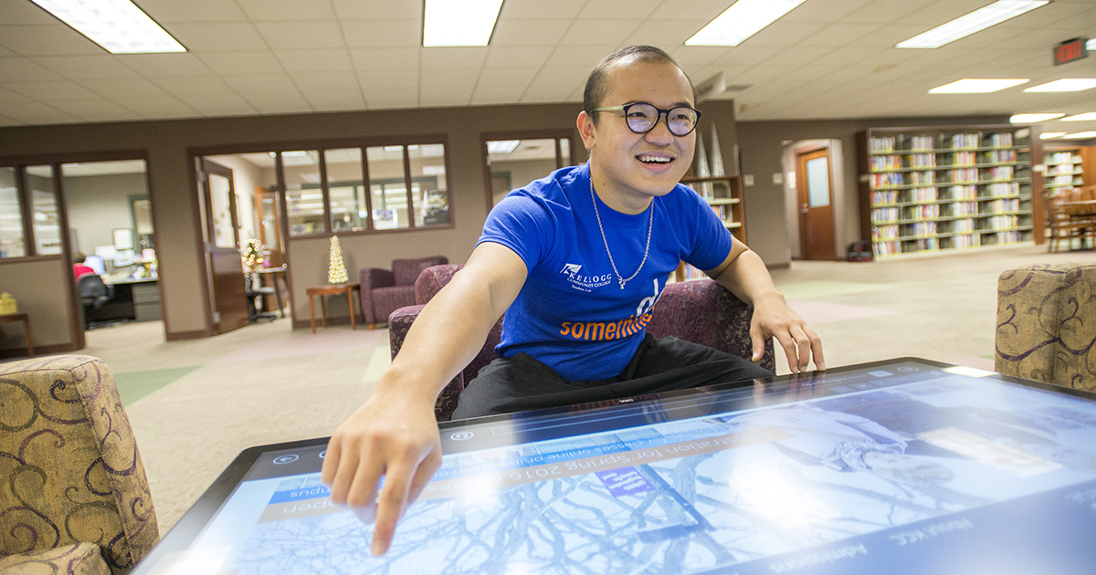 A student uses a giant touchscreen device in the library.
